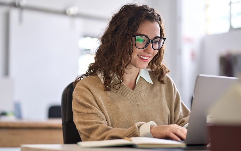 women smiling looking at computer wearing brown sweater and glasses
